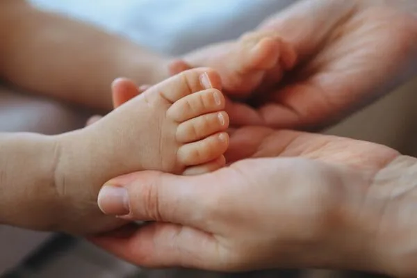 Les pieds du bébé sont enveloppées par les mains de la réflexologue qui effectue un massage circulaire à l'aide de ses pouces