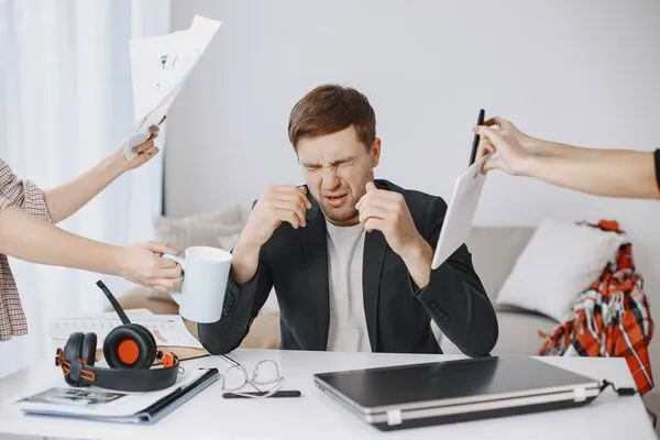 Un homme débordé et stressé au travail avec des mains qui lui tendent des papiers à signer, son café